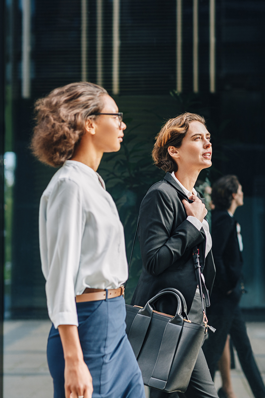 Two businesswomen walking to the office carrying her bags and talking