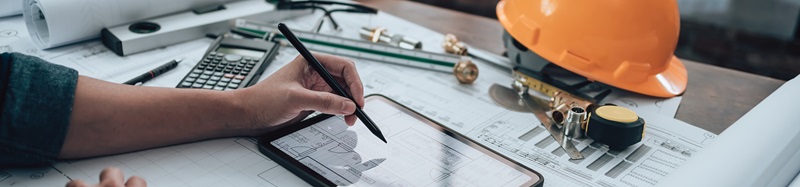 Engineering working with drawings inspection on tablet in the office and Calculator, triangle ruler, safety glasses, compass, verniear caliper on Blueprint