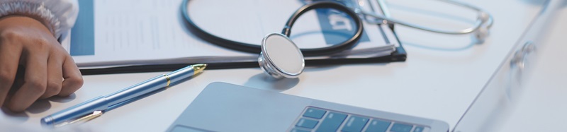A doctor in scrubs is working and reading medical research on their laptop in her office at a hospital